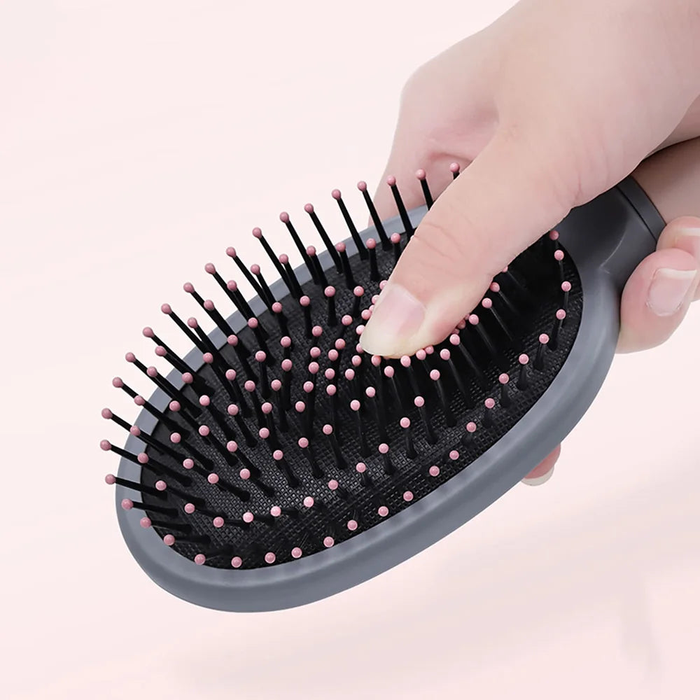 Hand holding a black Detangling Hair Brush with pink bristles on a light pink background