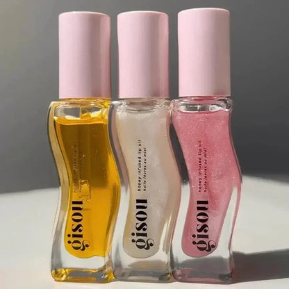 Three lip oil bottles with pink caps from the brand 'gisou' on a neutral background.