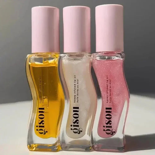 Three lip oil bottles with pink caps from the brand 'gisou' on a neutral background.