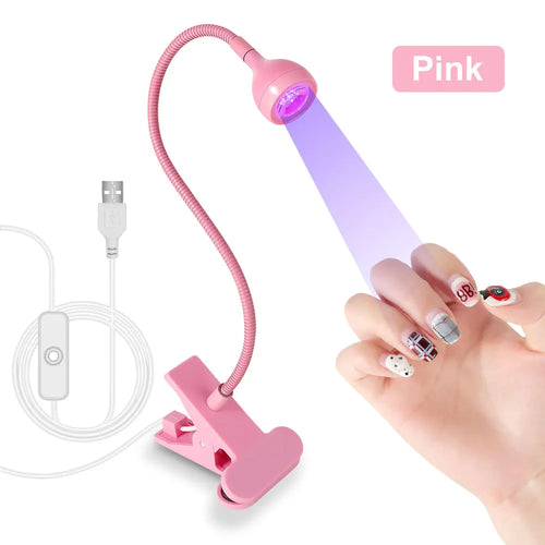 Pink UV/LED nail lamp with USB cable and a hand holding a nail, on a white background.